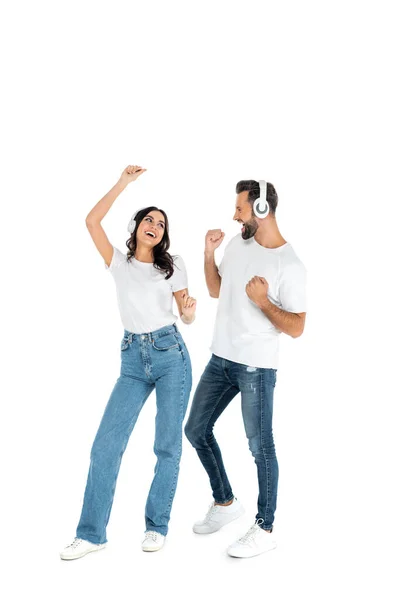 Full length view of excited couple in headphones and jeans dancing on white — стоковое фото