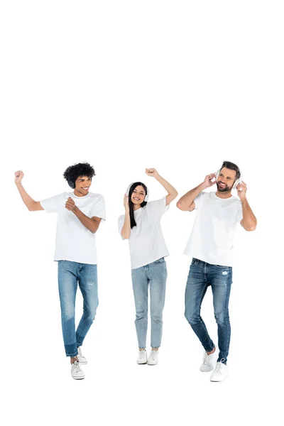 Vista completa de los hombres interracial y mujer asiática bailando en auriculares en blanco - foto de stock