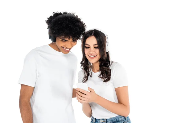 Lächelndes multiethnisches Paar mit Kopfhörern, das auf weißes Handy schaut — Stockfoto