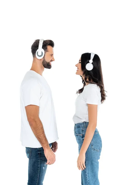 Side view of couple in t-shirts and headphones looking at each other isolated on white - foto de stock