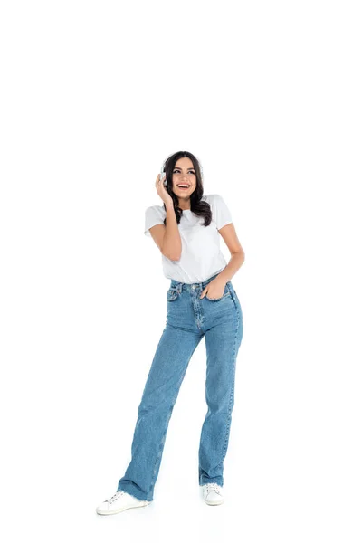 Full length view of happy woman in jeans listening music in headphones on white - foto de stock