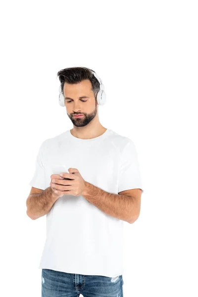 Homem em t-shirt e fones de ouvido usando telefone celular isolado em branco — Fotografia de Stock