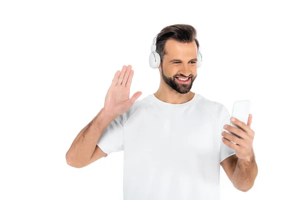 Gioioso uomo in cuffia agitando mano durante la videochiamata su smartphone isolato su bianco — Foto stock