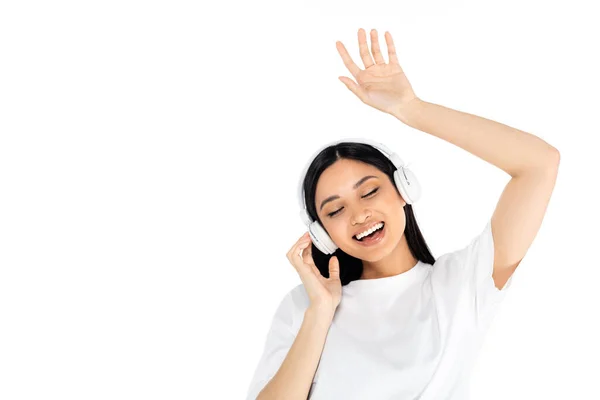Freudige asiatische Frau mit Kopfhörern tanzt mit geschlossenen Augen isoliert auf weiß — Stockfoto