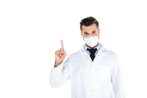 Doctor in white coat and medical mask looking at camera and pointing with finger on white — Stockfoto