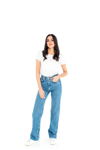 Full length view of young smiling woman standing with hand in pocket of jeans on white — Stockfoto