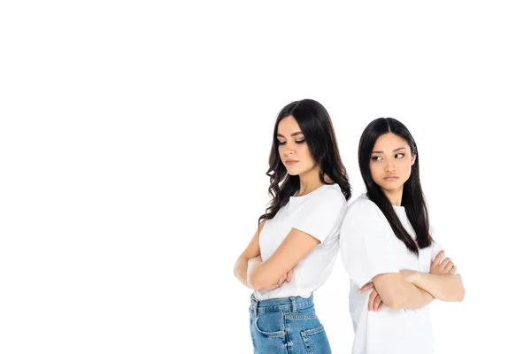 Offended interracial women standing back to back with crossed arms isolated on white — стоковое фото