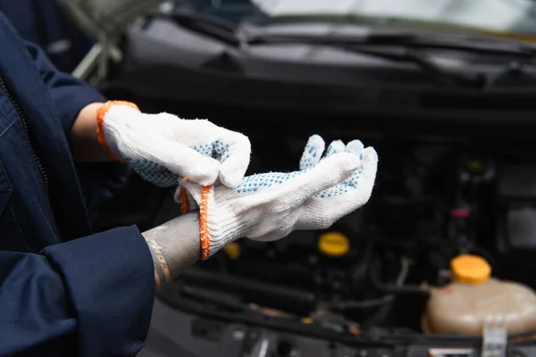 Vista recortada del mecánico con guantes cerca de coche borroso en el garaje - foto de stock