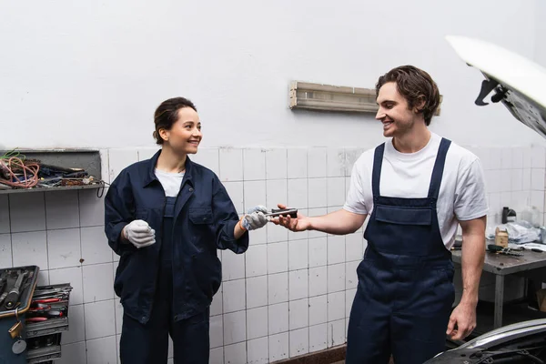 Smiling mechanics holding tool near car in service — Stock Photo