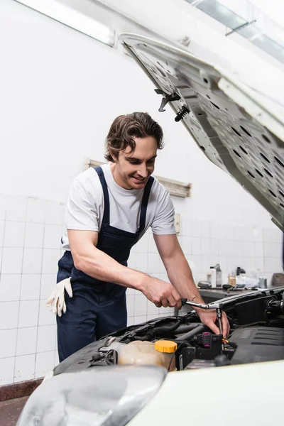 Mecânico positivo em chave de retenção uniforme enquanto trabalhava com carro em serviço — Fotografia de Stock