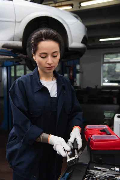 Trabajadora en guantes toma herramienta cerca de caja de herramientas en servicio de coche - foto de stock