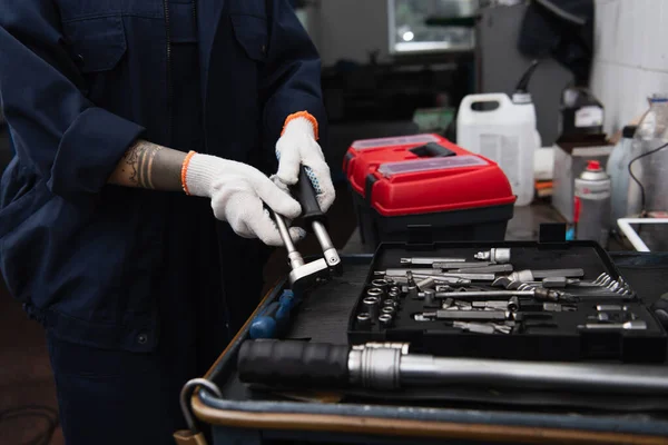 Cropped view of handywoman holding tool near wrenches in car service — стоковое фото