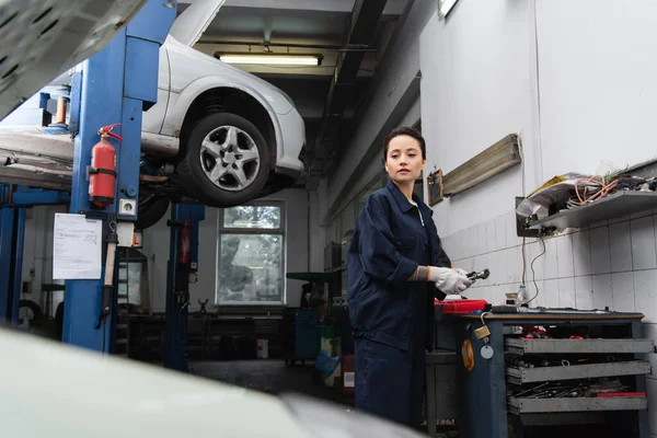 Mechanic holding tool and looking at blurred car in service — Stockfoto