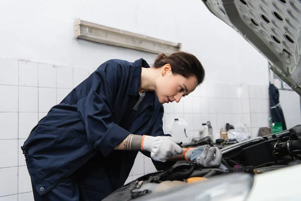 Mécanicien tatoué à l'aide d'une clé tout en travaillant avec l'automobile en service — Photo de stock