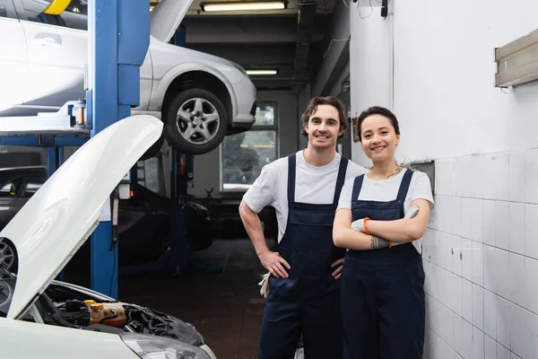 Cheerful mechanic in uniform looking at camera near car in garage — Stock Photo