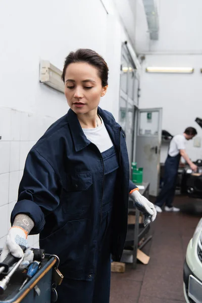 Mechanic taking tool near blurred car in garage — Fotografia de Stock