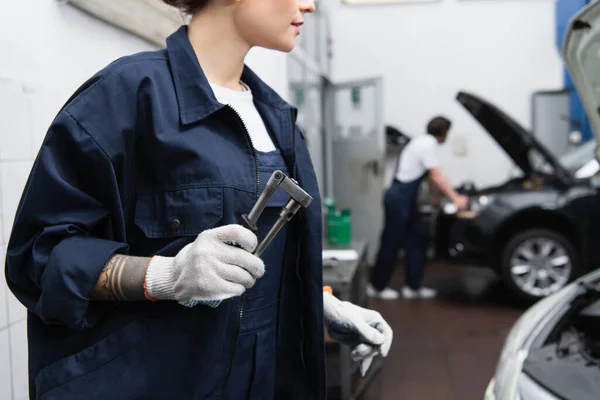 Ausgeschnittene Ansicht des Mechanikers in Uniform und Handschuhen, die Werkzeug im Autoservice halten — Stockfoto