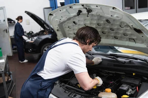 Foreman in gloves and overalls working with car with open hood in garage — Stock Photo