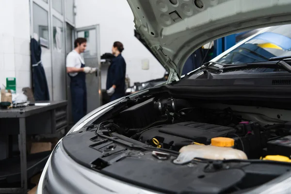 Car with open hood near blurred mechanics in garage — Foto stock