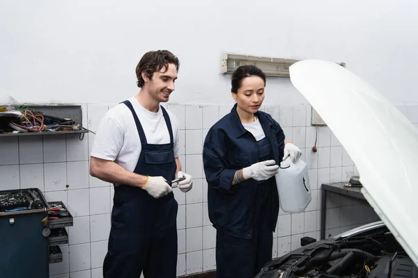 Mechanic holding canister near smiling colleague and car in garage — Stock Photo