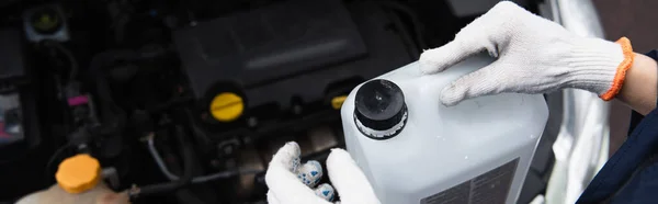 Top view of mechanic in gloves holding canister near blurred car in garage, banner — Stock Photo