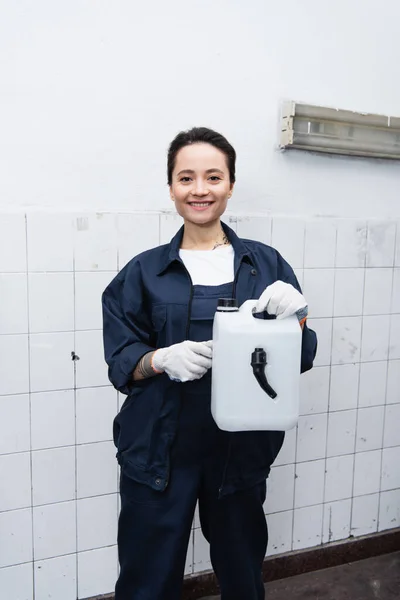 Mecánico sonriente en contenedor de sujeción uniforme en servicio de automóvil - foto de stock