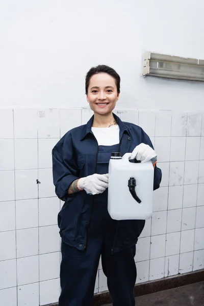 Smiling mechanic in uniform holding canister in car service — стоковое фото