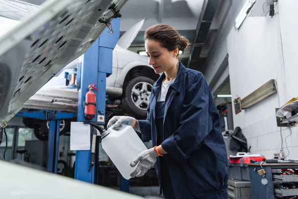 Young mechanic in gloves holding canister near auto in garage — Stockfoto