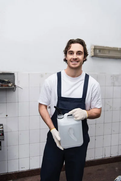 Positiver Mechaniker in Handschuhen und Overalls hält Kanister in Garage — Stockfoto