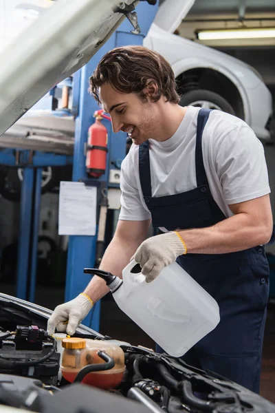 Vista lateral do reparador alegre segurando recipiente perto de automóvel na garagem — Fotografia de Stock