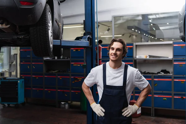 Усміхнений механік тримає руки на стегнах в гаражі — стокове фото