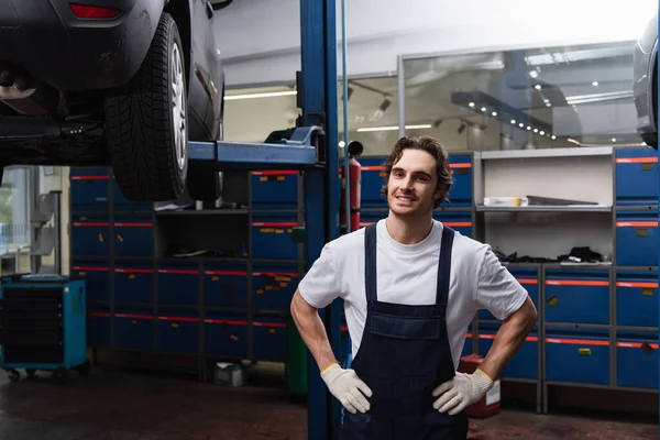 Smiling mechanic holding hands on hips in garage — стоковое фото