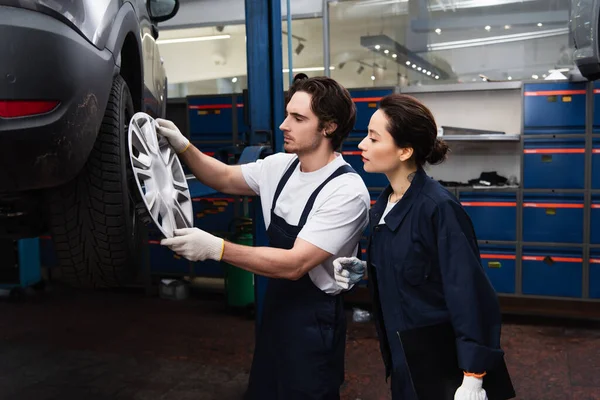 Side view of mechanics in gloves looking at wheel disk near car in service — Stock Photo