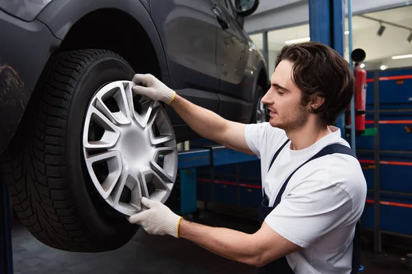 Side view of mechanic holding wheel disk near auto in garage — стоковое фото