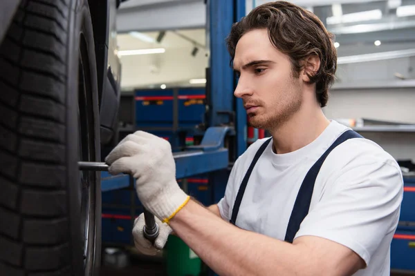 Mechanic using wrench on wheel of car in garage — Stockfoto