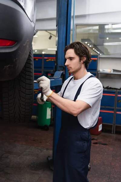 Mechanic with wrench fixing wheel of car in service — Stockfoto
