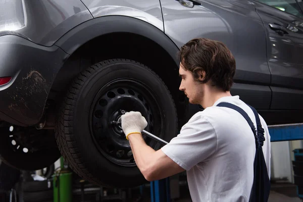 Vue latérale de l'ouvrier dévissant roue de voiture dans le garage — Photo de stock