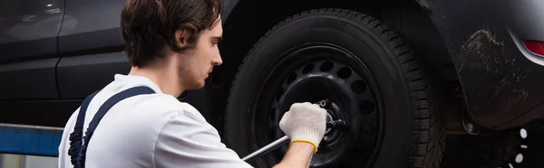 Side view of mechanic unscrewing car wheel in service, banner — Stock Photo