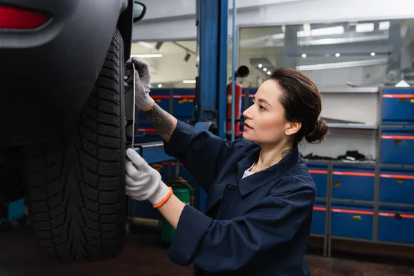 Young workwoman holding disk near wheel of blurred car in garage — Fotografia de Stock