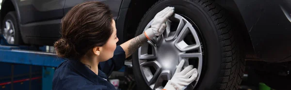 Young mechanic holding disk of car wheel in service, banner — Stock Photo