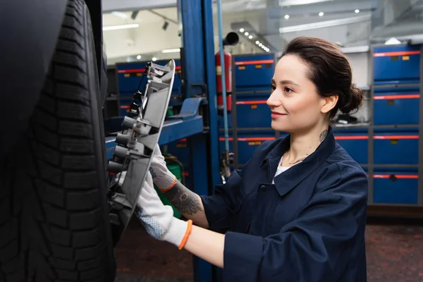 Smiling mechanic in gloves holding disk of car wheel in service — Stock Photo