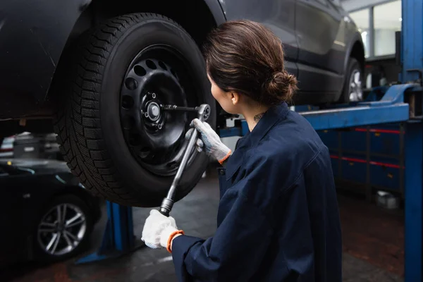 Tattooed mechanic working with wrench and car wheel in service — стоковое фото