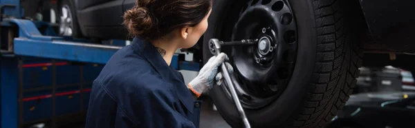 Workwoman in glove working with car wheel and wrench in garage, banner — Stockfoto