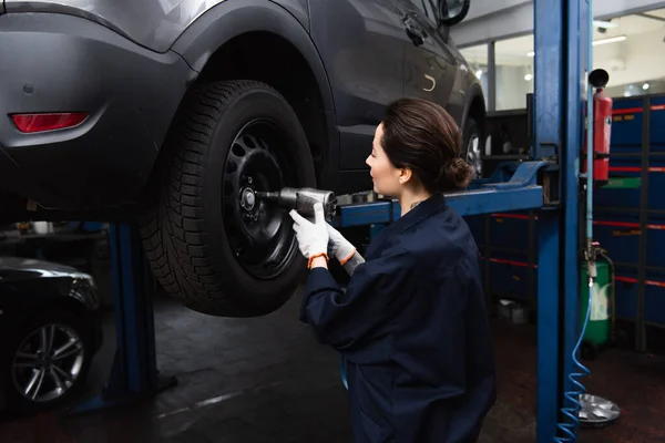 Side view of forewoman working with impact wrench on wheel of car in service — стоковое фото