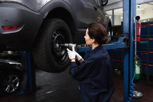 Vista lateral de la mujer que trabaja con llave de impacto en la rueda del coche en servicio - foto de stock