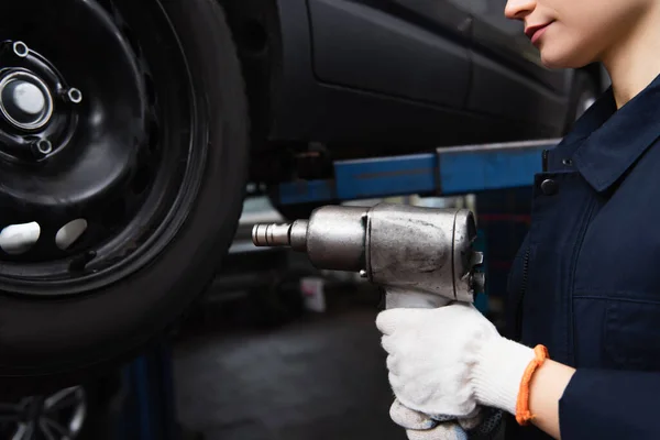 Vista recortada de mecánico en guantes que sostienen la llave de impacto cerca de auto en el garaje - foto de stock