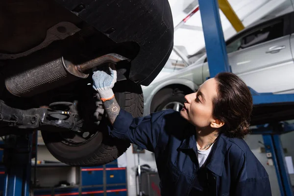 Young mechanic in glove standing near vehicle silencer in service — Fotografia de Stock
