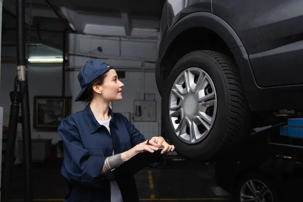 Vue latérale du mécanicien tatoué dans le presse-papiers de maintien de capuchon près de l'automobile en service — Photo de stock