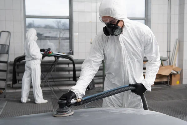 Workman in hazmat suit working with car polisher in garage — стоковое фото