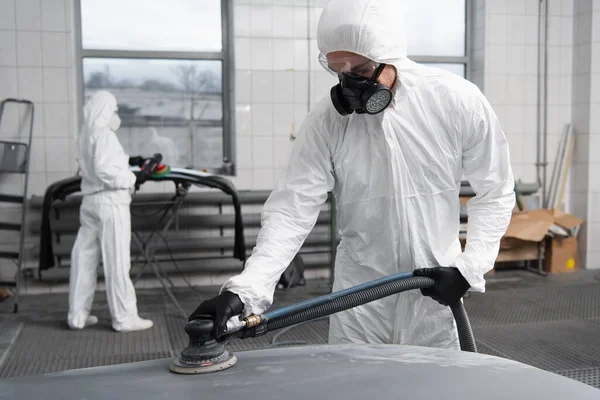 Ouvrier en combinaison Hazmat travaillant avec polisseuse de voiture dans le garage — Photo de stock